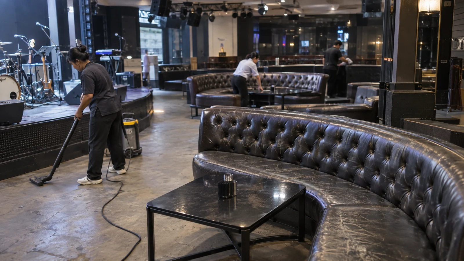 A long curved stage-side leather sofa in a Bangkok nightclub an hour before opening, with the house lights up and the floor being cleaned