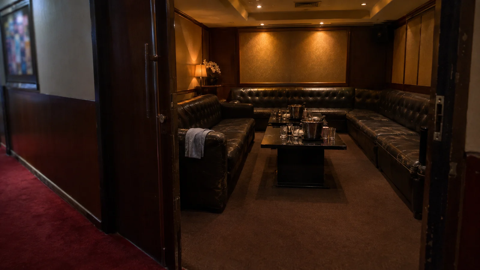 The doorway of a private party suite before opening, sofas set and lights low